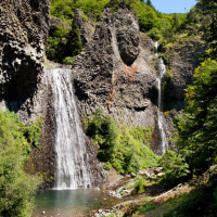 Waterfall cascading down rocky cliffs into a pool near Gluiras, Auvergne-Rhône-Alpes, France, surrounded by trees.