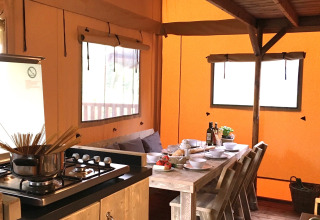 Alloggio glamping con cucina accogliente, lungo tavolo in legno e atmosfera interna da tenda.