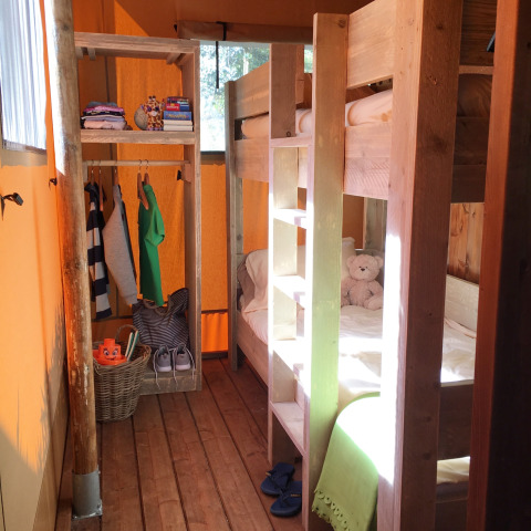 Gezellige glamping tent met houten stapelbedden, open garderobe en zonlicht op houten vloer.