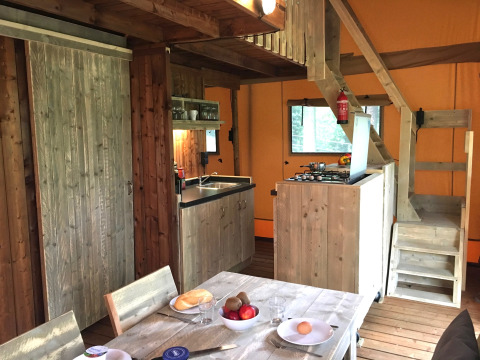 Vue intérieure d'un hébergement glamping avec cuisine, table à manger et escalier en bois vers la mezzanine.