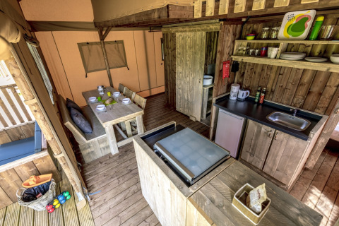 Interior de alojamiento glamping con cocina, mesa de comedor de madera y decoración rústica en tienda.