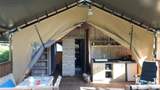 Vista interna di una tenda safari con pavimento in legno, cucina, zona pranzo e arredi accoglienti.