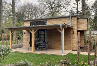 Modern tiny house met houten gevel, overdekte veranda, tuinset en omgeven door groen en bomen.