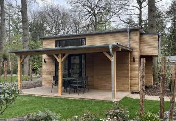Tiny house moderna in legno con veranda coperta, tavolo da esterno e circondata da prati verdi.