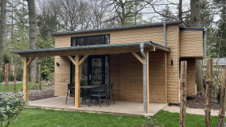 Tiny house moderna in legno con veranda coperta, tavolo da esterno e circondata da prati verdi.