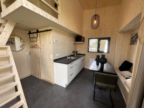 Modern tiny house interieur met licht hout, kitchenette, eethoek, slaaploft en minimalistisch decor.