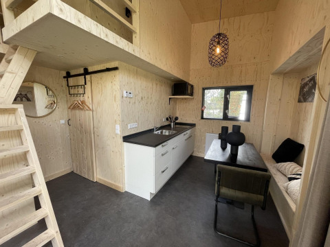 Moderne tiny house interiør med lyst træ, tekøkken, spiseplads, hems og minimalistisk indretning.