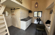 Moderne tiny house interiør med lyst træ, tekøkken, spiseplads, hems og minimalistisk indretning.