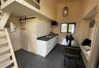 Interior moderno de tiny house con madera clara, cocina, comedor, altillo y decoración minimalista.