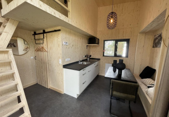 Intérieur de tiny house moderne avec bois clair, kitchenette, coin repas, mezzanine et déco minimaliste.