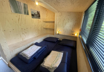 Dormitorio en casa pequeña con cama doble, paredes de madera, lámparas, ventana y ambiente acogedor.