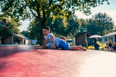 Twee blije kinderen spelen op een springkussen voor tiny houses met bomen en gezinnen eromheen.