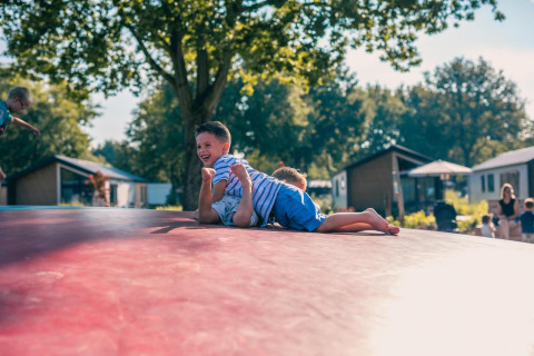 Twee blije kinderen spelen op een springkussen voor tiny houses met bomen en gezinnen eromheen.