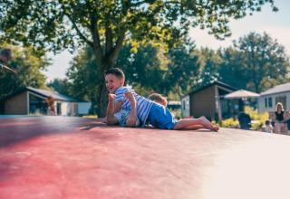 Zwei lachende Kinder spielen auf einem Luftkissen vor Tiny Houses und Bäumen im Hintergrund.