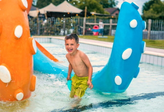 Lachende jongen speelt in kinderbad met kleurrijk speelgoed bij een tiny house in de zomer.