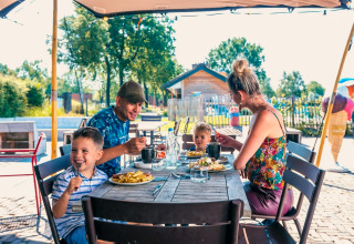 Gezin geniet van lunch buiten aan tafel voor een Tiny House in Kaatsheuvel, Nederland, op zonnige dag.