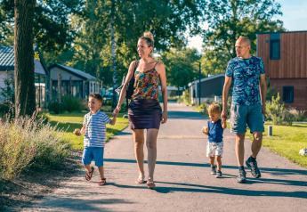 Familia caminando en un sendero soleado cerca de una Tiny House en Kaatsheuvel, Países Bajos, rodeados de naturaleza.