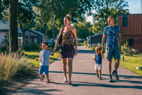 Gezin wandelt samen op zonnige weg naast Tiny House in Kaatsheuvel, Nederland, omringd door zomerse natuur.