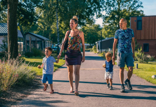 Familie spaziert bei Sonnenschein nahe Tiny House in Kaatsheuvel, Niederlande, durch eine grüne Wohnsiedlung.