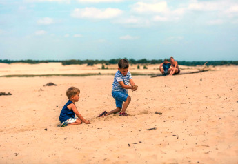 Dos niños juegan en la arena cerca de la Tiny House en Kaatsheuvel, Países Bajos, padres al fondo sentados.