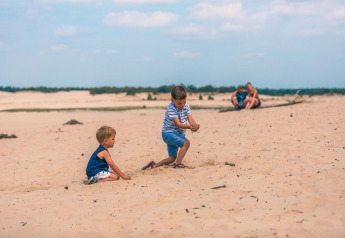 Zwei Kinder spielen im Sand bei Tiny House in Kaatsheuvel, Niederlande, Eltern sitzen im Hintergrund.