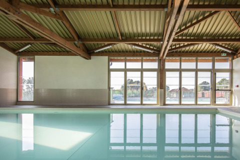 Indendørs swimmingpool med store vinduer og synlige træbjælker i Arden Parks - Signy l'Abbaye, Frankrig.