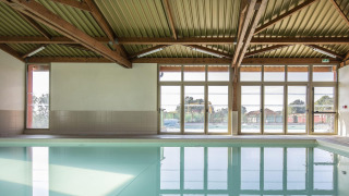 Piscina cubierta con vigas de madera y grandes ventanales en Arden Parks - Signy l'Abbaye, Grand Est, Francia.