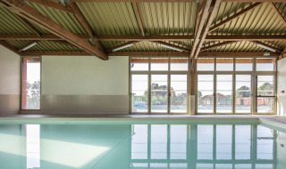 Piscina cubierta con vigas de madera y grandes ventanales en Arden Parks - Signy l'Abbaye, Grand Est, Francia.