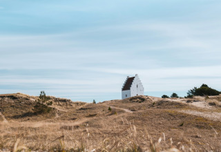 Un edificio bianco solitario si trova tra dune erbose sotto un cielo azzurro vicino a Hirtshals, Jutland settentrionale.