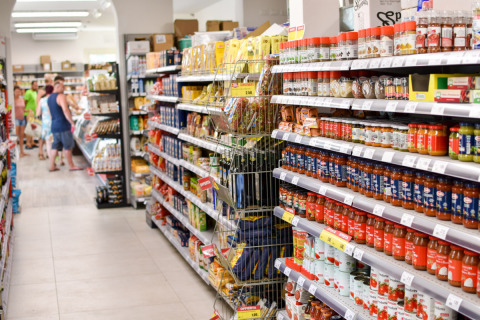 Pasillo de supermercado en Vigna sul Mar Family Camping Village, Italia, con estantes llenos y personas.