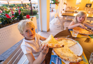 Twee kinderen eten buiten pizza bij Vigna sul Mar Family Camping Village in Emilia-Romagna, Italië.