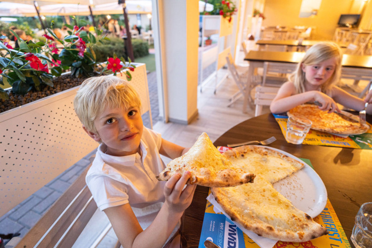 Twee kinderen eten pizza op het terras van Vigna sul Mar Family Camping Village in Emilia-Romagna, Italië.