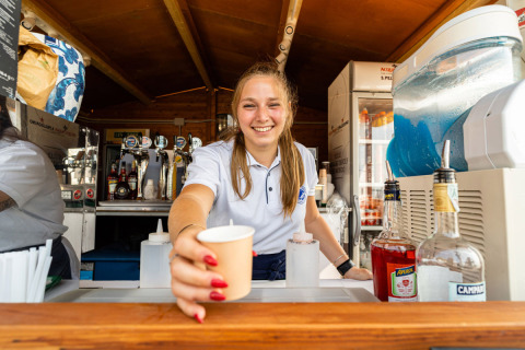 Freundliche Frau reicht ein Getränk an der Bar im Vigna sul Mar Family Camping Village in Emilia-Romagna, Italien.