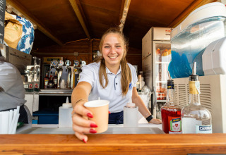 Glad kvinde serverer en drink i barområdet på Vigna sul Mar Family Camping Village i Emilia-Romagna, Italien.