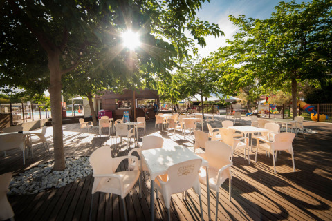 Zona de asientos al aire libre con mesas y sillas bajo árboles en Vigna sul Mar Family Camping Village, Italia.
