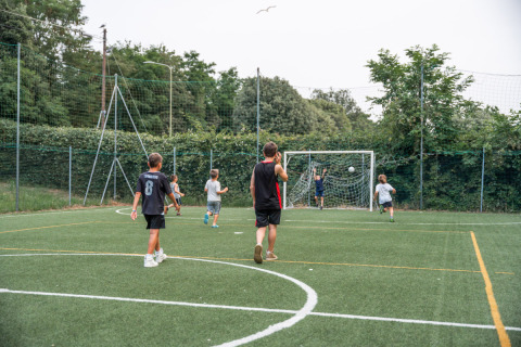 Kinder und ein Erwachsener spielen Fußball auf einem grünen Platz im Vigna sul Mar Family Camping Village.
