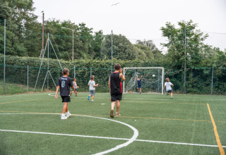 Børn og en voksen spiller fodbold på en grøn bane i Vigna sul Mar Family Camping Village, Italien.