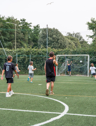 Niños y un adulto juegan al fútbol en un campo verde en Vigna sul Mar Family Camping Village, Italia.
