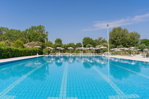 Groot openluchtzwembad bij Vigna sul Mar Family Camping Village in Emilia-Romagna, omringd door parasols.