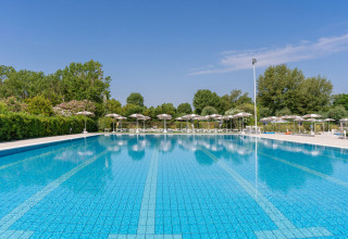 Stort udendørs svømmebassin ved Vigna sul Mar Family Camping Village i Emilia-Romagna, omgivet af parasoller.