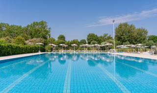Gran piscina al aire libre en Vigna sul Mar Family Camping Village en Emilia-Romaña, rodeada de sombrillas.