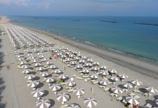 Luchtfoto van een zandstrand met rijen parasols bij Vigna sul Mar Family Camping Village, Emilia-Romagna, Italië.