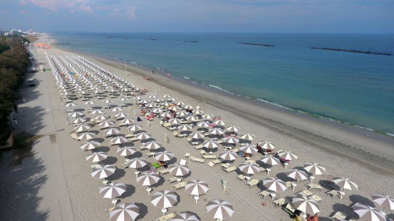 Luchtfoto van een zandstrand met rijen parasols bij Vigna sul Mar Family Camping Village, Emilia-Romagna, Italië.