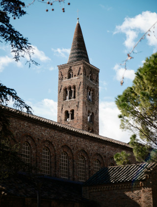 Un histórico campanario en Emilia-Romaña, Italia, rodeado de árboles verdes y cielo con nubes.