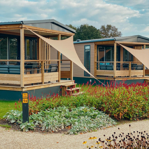 Moderne Tiny Lodge op Holiday park De Boshoek in Nederland met houten terras en kleurrijke bloementuin.