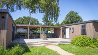 Outdoor photo of Family Lodge featuring a wooden deck with seating, greenery and bright sunny skies.