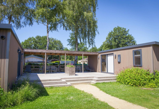 Foto exterior de Family Lodge con terraza de madera, muebles de jardín y vegetación en un día soleado.
