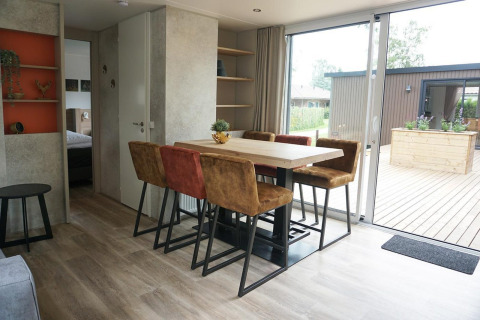 Dining area with six chairs and terrace view inside Family Lodge at Holiday park De Boshoek, Netherlands.