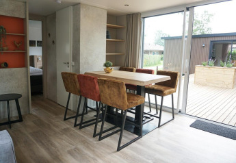 Dining area with six chairs and terrace view inside Family Lodge at Holiday park De Boshoek, Netherlands.