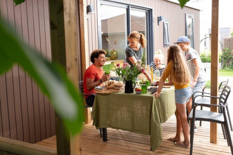 Familie isst gemeinsam auf einer Terrasse einer Family Lodge im Holiday park De Boshoek, Niederlande.